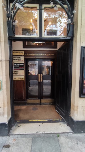 From sidewalk facing venue. A very small step before a black door. Push to left to open.