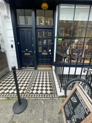 From street, facing venue. Small bump ahead. Path straight. Blue glass and wooden door at end of path. Gold knob to right. Push to open.