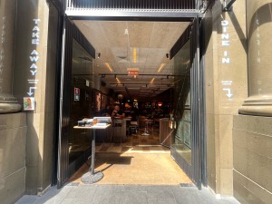 Glass double doors with black metal frame. Push from middle. Reception desks obstructing on left, and on right after door.
