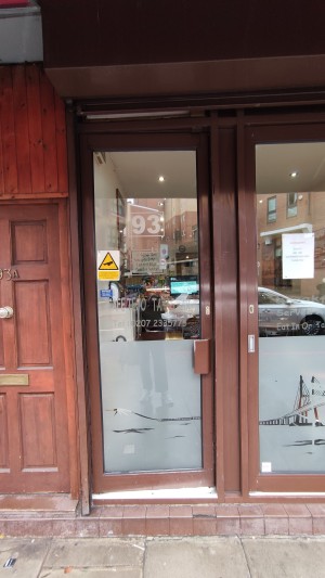Glass door with brown wooden frames. Push brown handle on right to open. One step up to door.