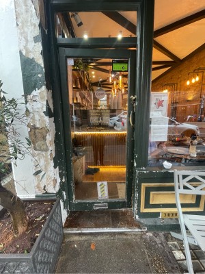 Glass door with green wooden frame ahead. Gold metal handle to right. Push to open. Planter to left.