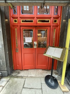Double glass and wooden red doors ahead. Gold metal panel to centre. Push to open.