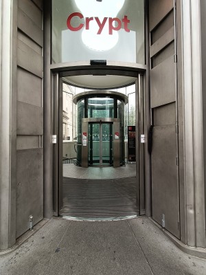 From street, facing venue. Glass doors with silver frame. Doors automatically open.
