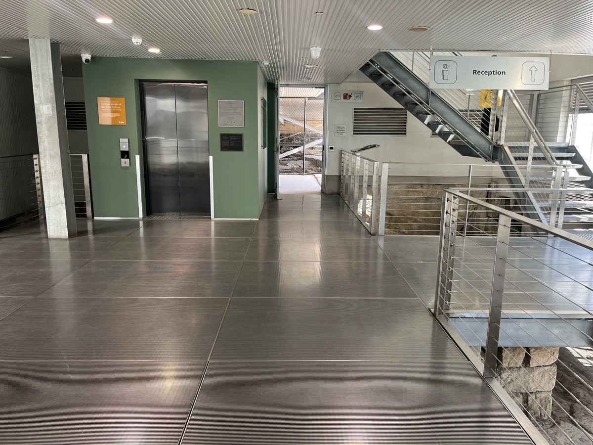 From top of ramp facing right. Lift on wall ahead to left. Path to staircase continues right ahead.