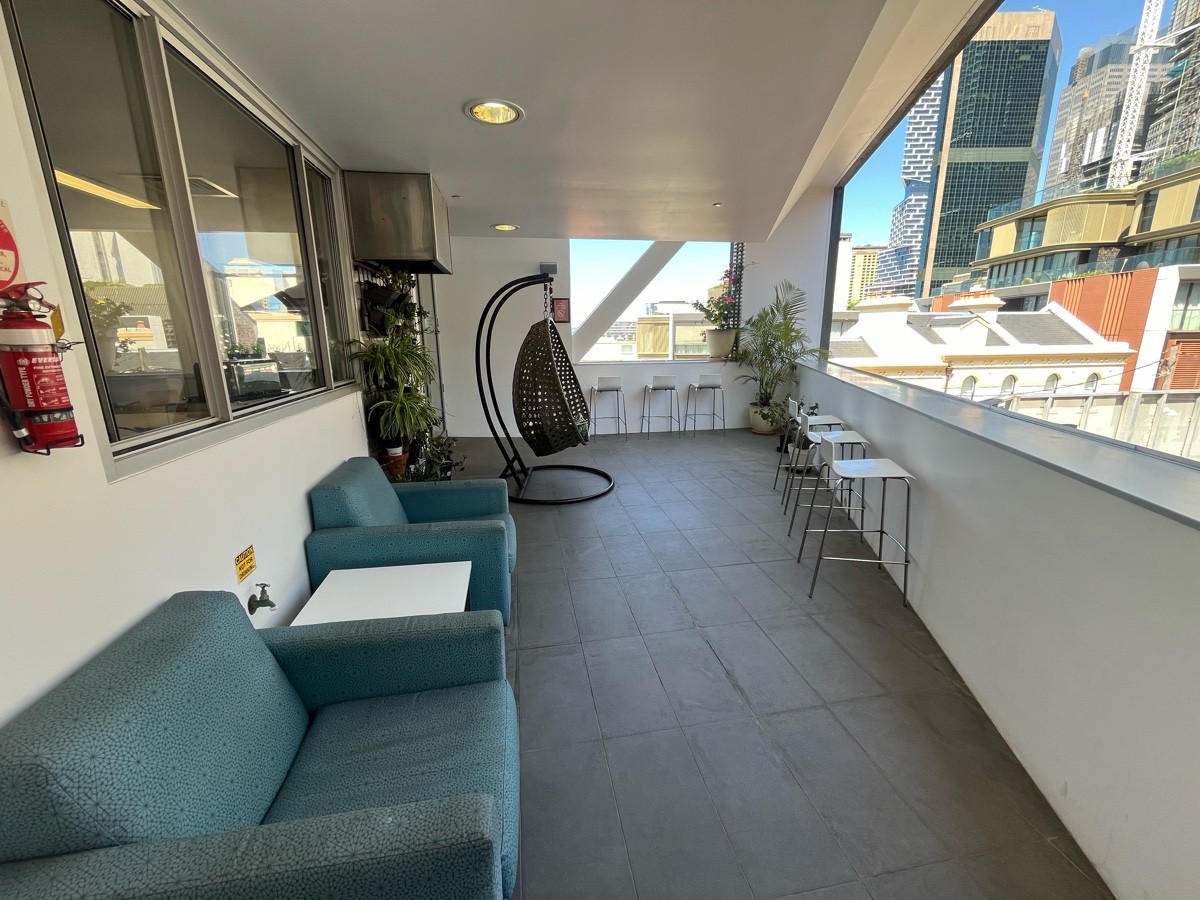 From door facing straight. Armchairs with low table on left followed by swing. High balcony seating with backed stools along right wall and wall ahead