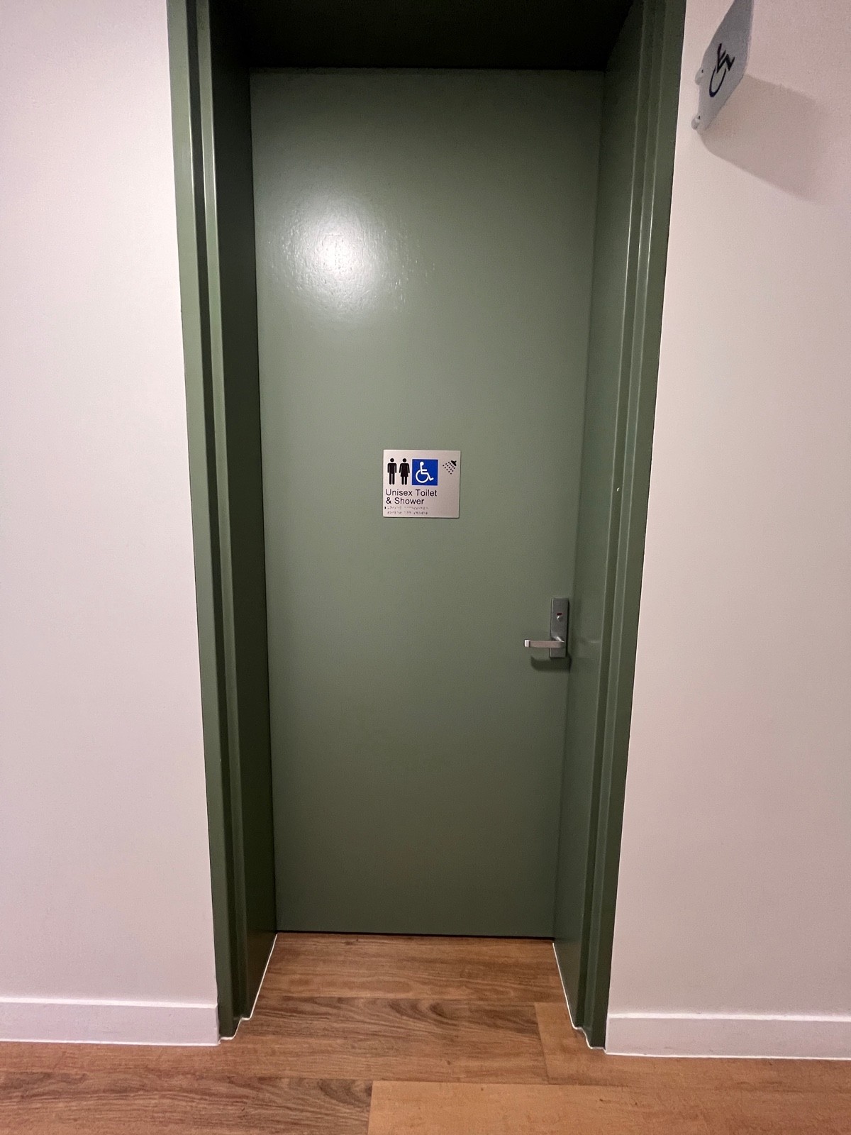 From path facing left. Green wooden bathroom door. Turn handle and push from right.