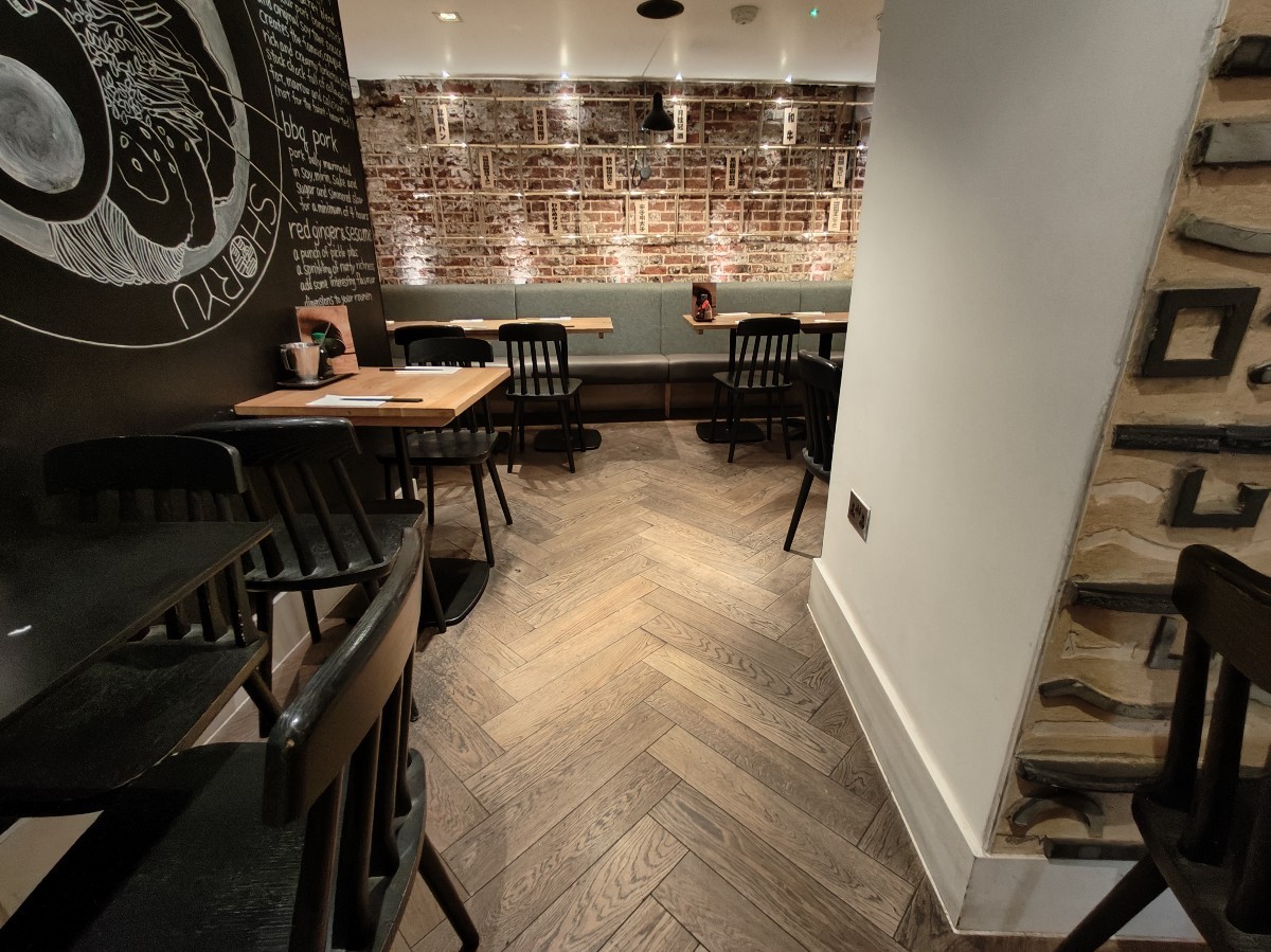 From left of table and chairs after front area facing straight. Tables and chairs along left. Path ahead to half booth at back.