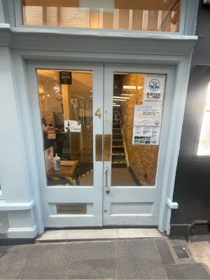 Light blue and glass-panelled doors ahead. Gold metal panels in centre. Silver metal vertical handle underneath it on right door. Push to open.