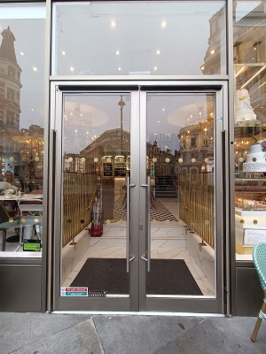 Glass doors with grey frame. Silver, metal, vertical handles in middle. Push to open.