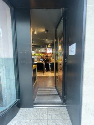Glass door with black frame ahead. Gold vertical metal handle to left. Push to open.