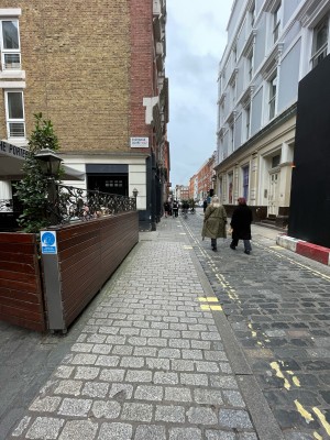 From outside main entrance, facing right. Wooden fence along left. Pavement ahead, going straight.