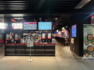Open archway to venue. Ordering screens ahead to left. Path ahead to right.