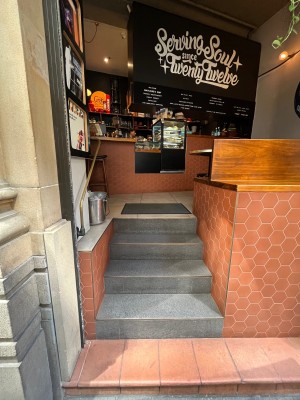 Open archway from street to venue. 5 steps up through archway ahead. Handrail on left. Doormat at top.