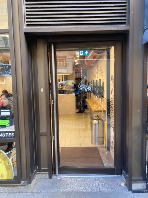 Single glass door with brown frame ahead. Push to open via vertical metal handrail on left.