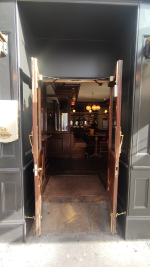 Glass doors with wooden frames ahead. Pull gold vertical handles in centre to open.