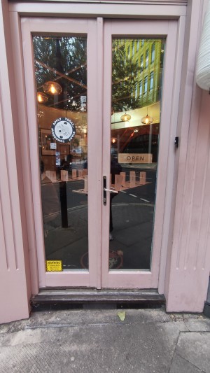 Glass doors with pink frames ahead. Push metal handle in centre to open.