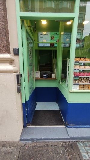 One step up to glass door with green frames. Push to right to open.