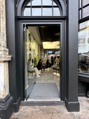 Glass door with black frame. Push from right to open.