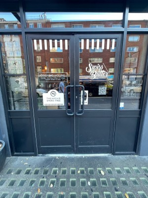 Glass doors with black frame ahead. Black vertical metal handles in centre. Push to open.