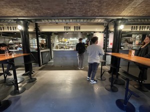 From inside the market facing venue. Path ahead to venue. High tables and stools on either side.
