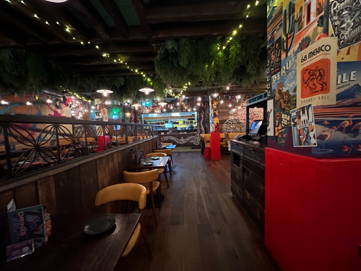 From divider facing straight. Path straight to open kitchen. Tables and chairs along left. Pillar right. Staff station beyond.