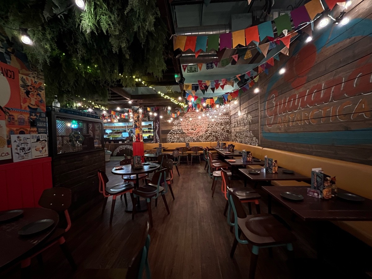 From half booth facing left. Path ahead to half booth on back wall. Half booth along right wall. Tables and chairs along left.