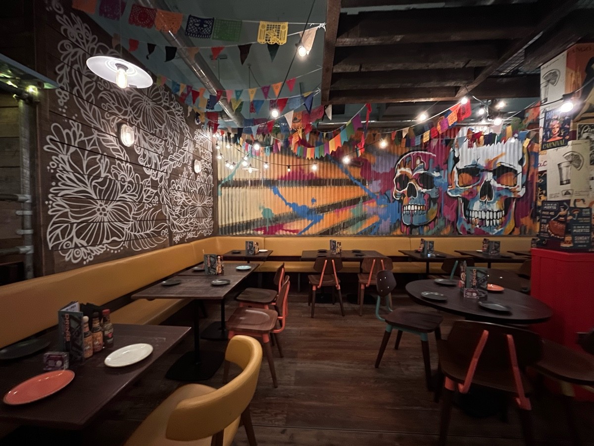 From divider facing left. Path ahead to half booth at back wall. Half booth along left. Table and chairs right.