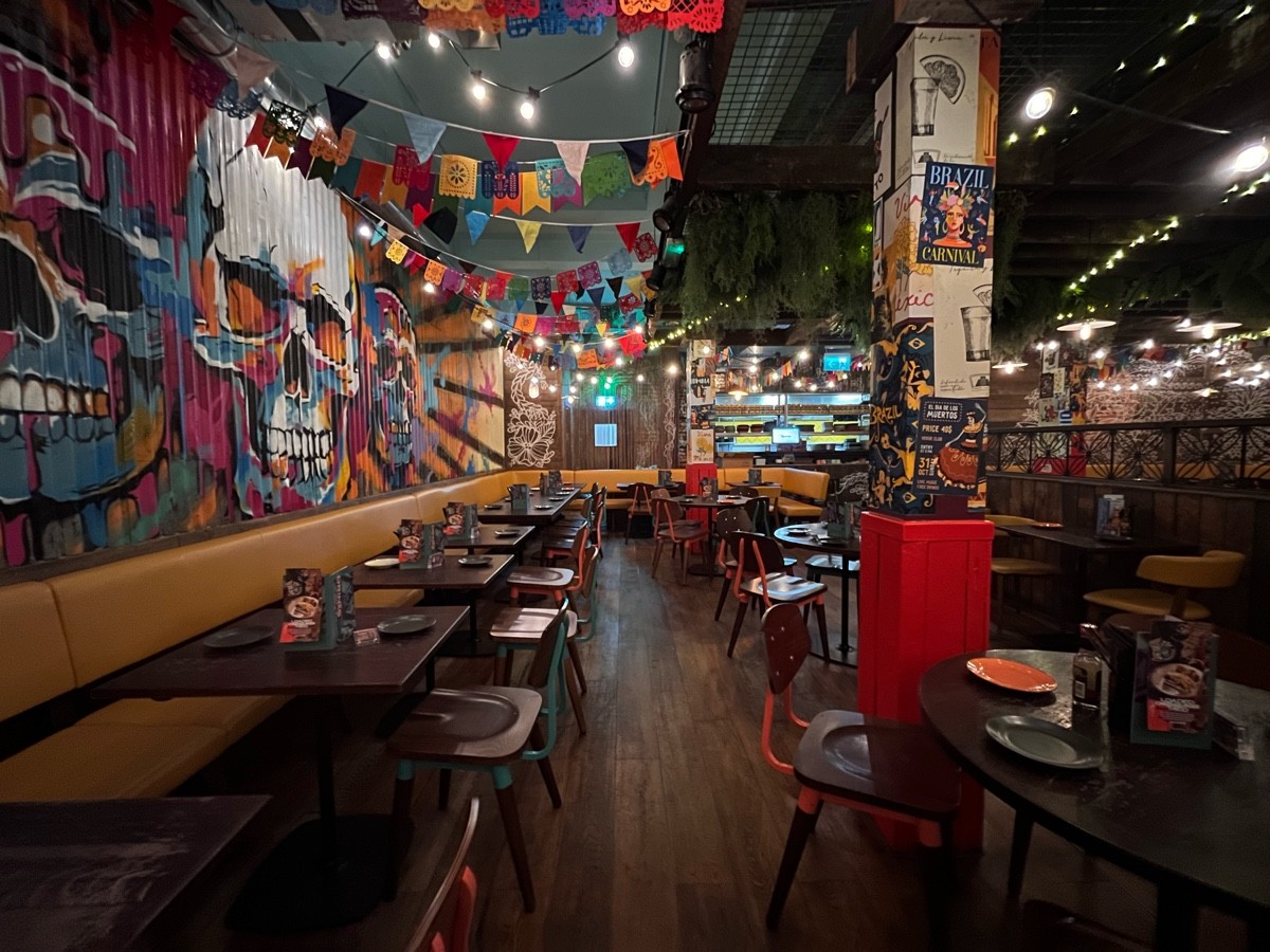 From half booth facing right. Path straight to half booth at back. Half booth along left. Tables and chairs along right.