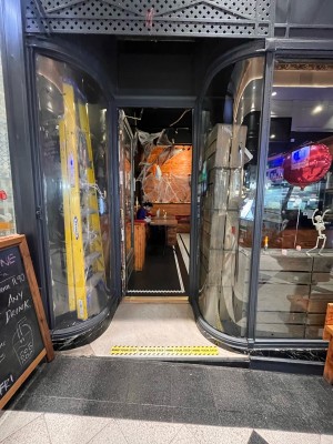 Single glass door in grey metal frame set back from pavement. Push gold metal handle from right. Sandwich board left.