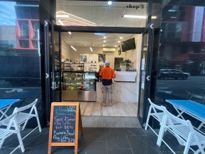 Glass double doors with black wooden frame fold open from middle. Central signage obstructing path to door.