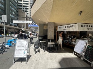 Open archway from street with no door. Kiosk counter on right wall ahead. Seating ahead and to right. Built in ramp down to area.