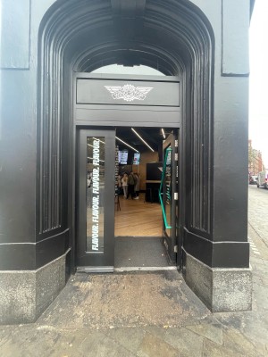 Glass door with black frame ahead. Green metal handle diagonally placed on door. Push to open.
