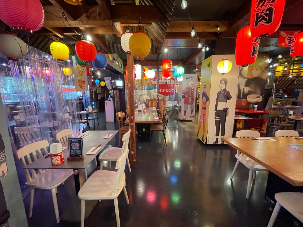 From end of tables and stools, facing right. Path straight. Table and chairs to left and right. Pillar ahead to left and right. Back area to far left.