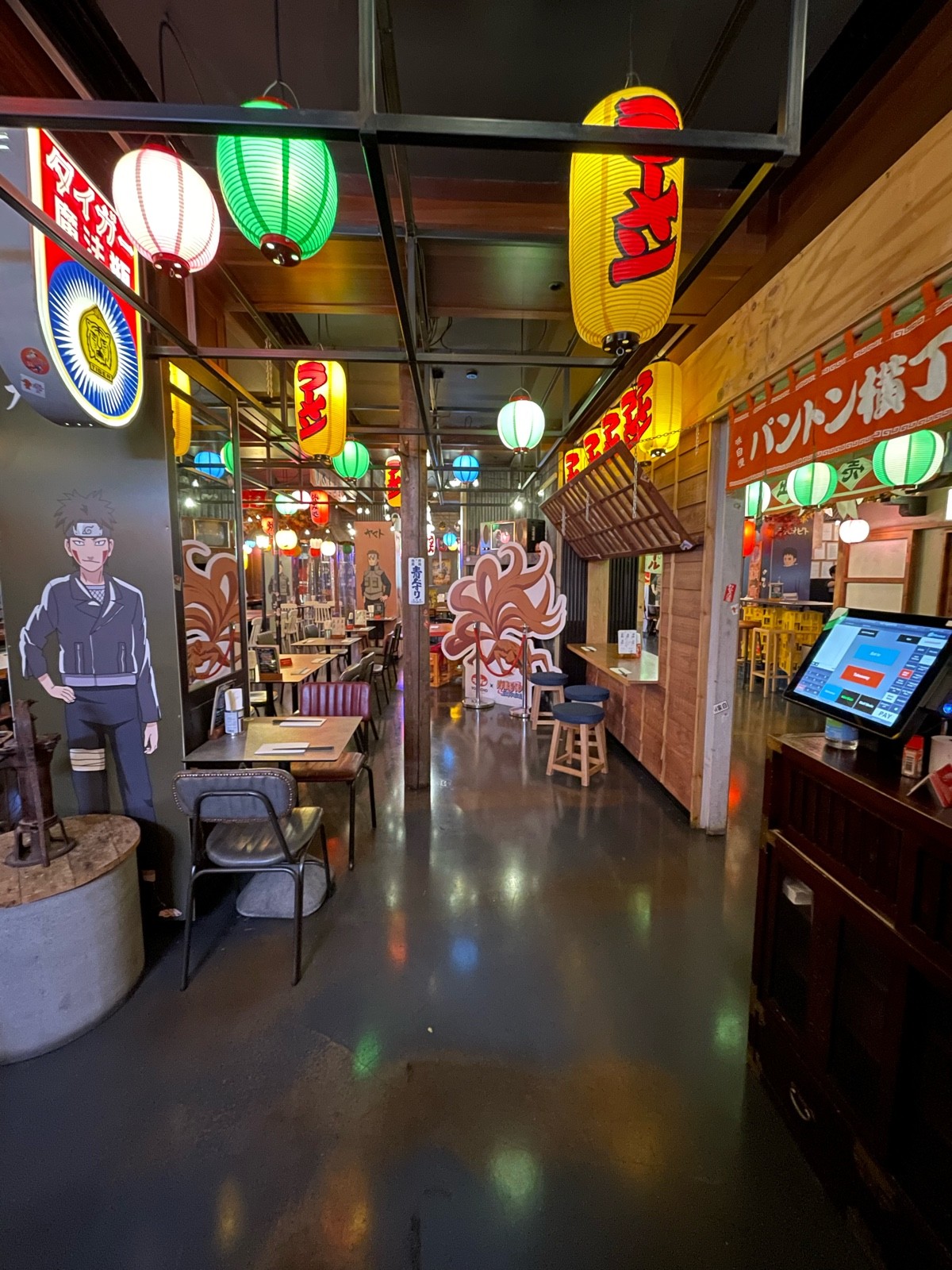 From lantern stand, facing right. Path straight. Pillar ahead in path and to left. Tables and chairs along left.