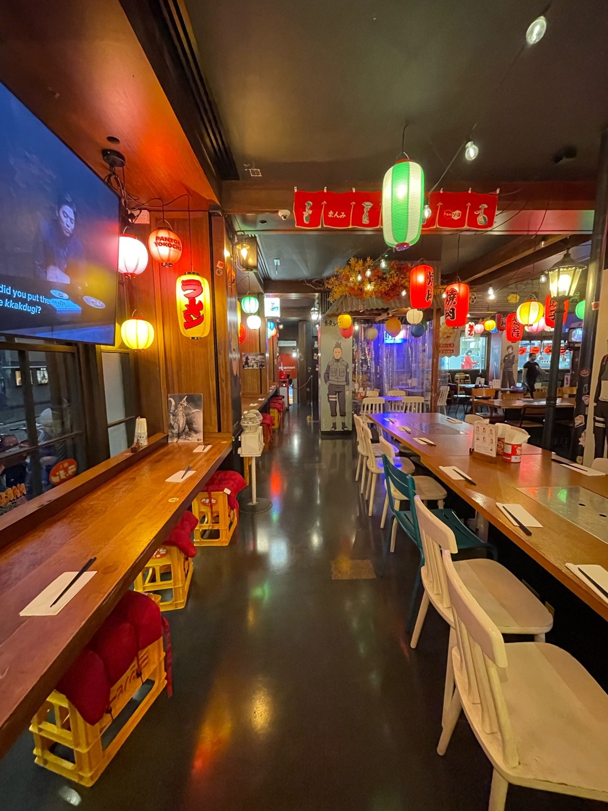 From left of long table, facing straight. Tables and stools along left with pillars in between. Long table and chairs along right.