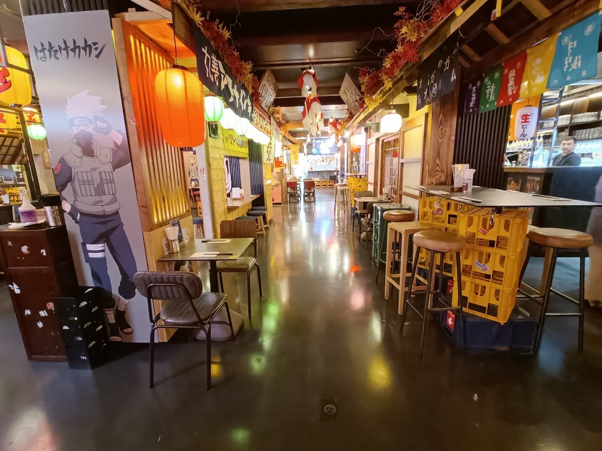 From left tables and stools, looking right. Tables and chairs on left. Tables and stools behind. High tables and stools along right. Path in middle.