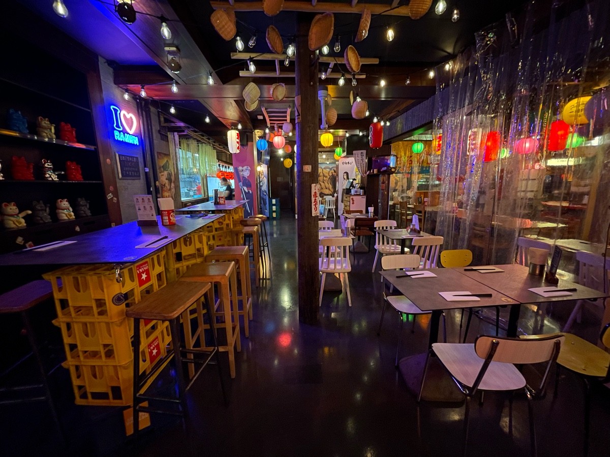 From end of tables and stools, facing right. Path straight. Pillar ahead in path. High table and stools along left. Tables and chairs along right.