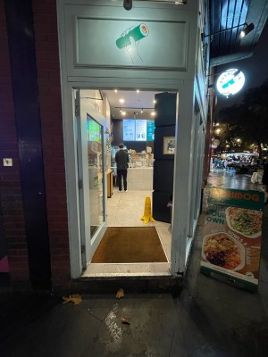 Glass door with light blue frame ahead. Silver metal panel to right. Push to open.