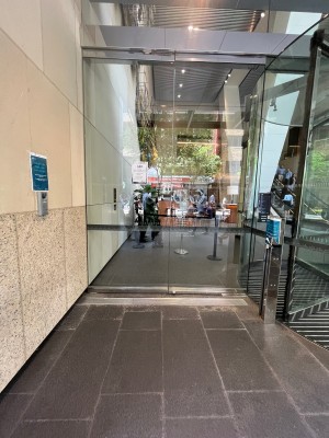 Glass door to left of revolving doors. Push button on right before door to open.
