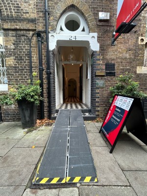 Preceding archway with steps before doorway. Planter on left and right, notice board right. Portable ramp available.