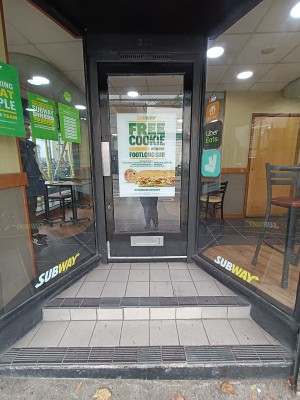 Glass door with black frame. Silver, metal pad on left. Push to open.