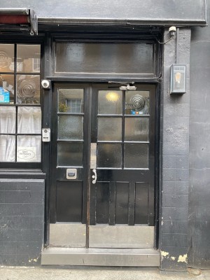 Single glass door with black frames ahead. Push to open via metal handle on left.
