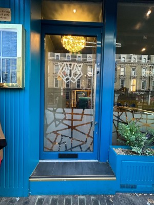 Glass door with bright blue frame and silver handle on right. Push to open.