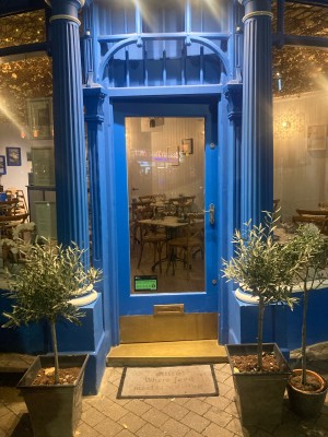 Path ahead with planters to each sides to glass door with blue frame on back. Push to open via golden handle on right.