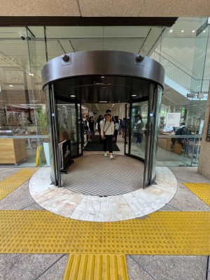 Glass doors with black metal frames slide open automatically from middle. Tactile flooring before doors. Doormat after.