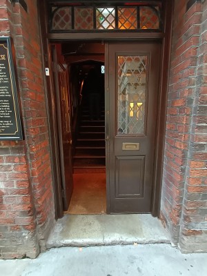 From sidewalk around corner to left of main entrance facing venue. Brown and glass paneled door. Push from centre to open.