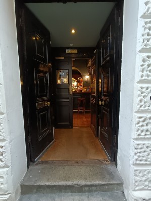 Black wooden doors with golden, metal handle in middle. Push to open.