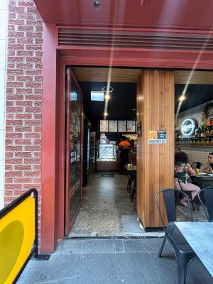 Glass door with red metal frame. Push from right to open. Restaurant barrier on left. Table and chairs on right.