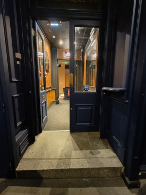 Facing opening to blue-framed glass doors. Push golden metal pads on centre to open.