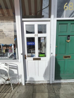 Facing white glass-panelled door. Push golden metal handle on left to open.